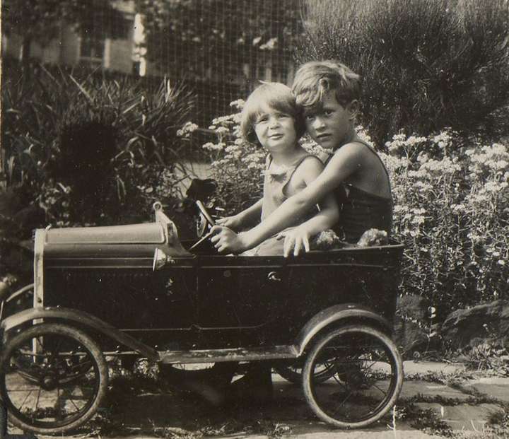 Black and white photo of a young Michael sitting in a toy car with his brother Peter in Croydon, 1933.